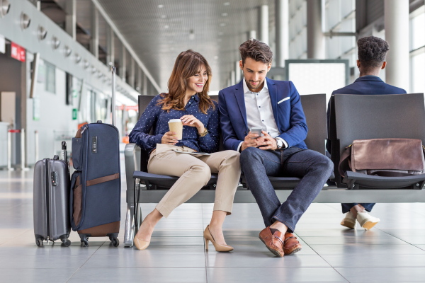 Two people sitting in airport looking at phone.